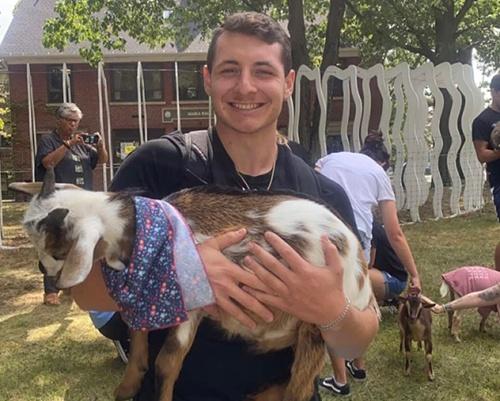 Young man smiling holding a goat.