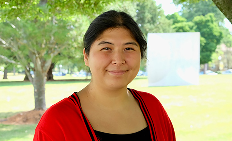 Young woman smiling wearing a black top with a red jacket with trees in the background