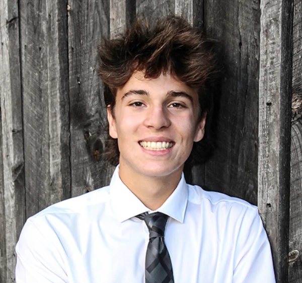 A young man wearing a dress shirt and tie against a fence