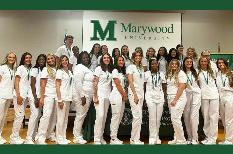 A group of nursing graduates from the Class of 2024 is pictured in nursing whites with a Marywood University banner behind them.