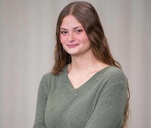 Young woman smiling wearing a green shirt with a grey backdrop.