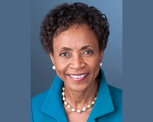 A smiling Dr. Bernadette Gray-Little wearing a blue blazer, pearl earrings, and a necklace.