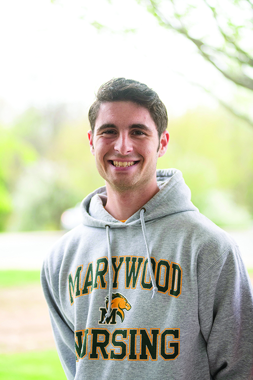 A man with short hair smiling, wearing a grey hoodie with 