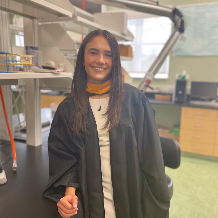 A female student wearing a commencement gown in a science lab.