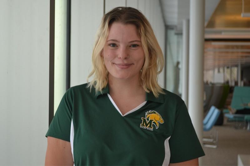 Young woman smiling wearing a green marywood shirt in a library.