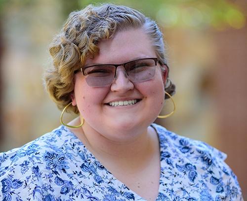 Young woman closeup wearing a blue and white shirt, black sunglasses, and gold earrings.