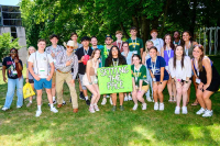 A large group of students is pictured outside on the Campus Green with a sign that says 