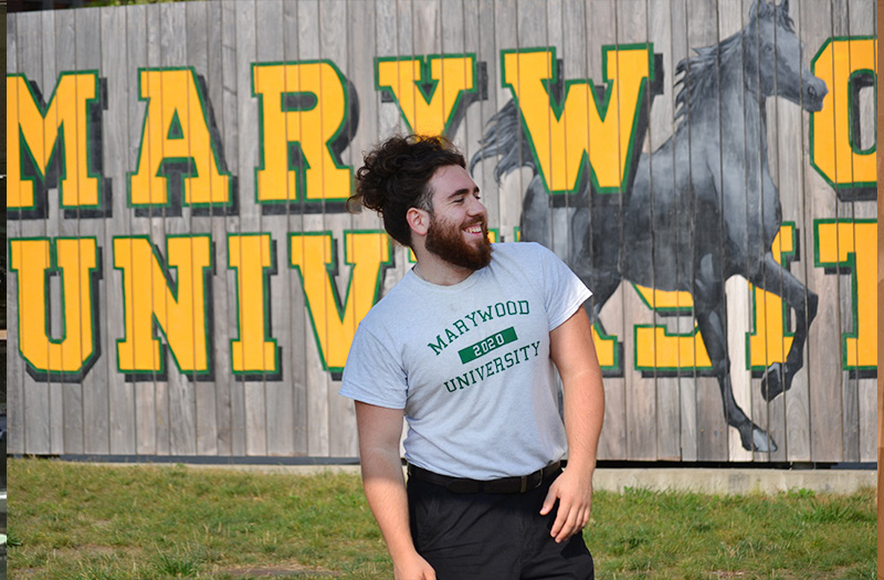 A man laughing standing in front of painted fence that reads 