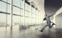 Businessman kicking a a soccer ball in an office setting.