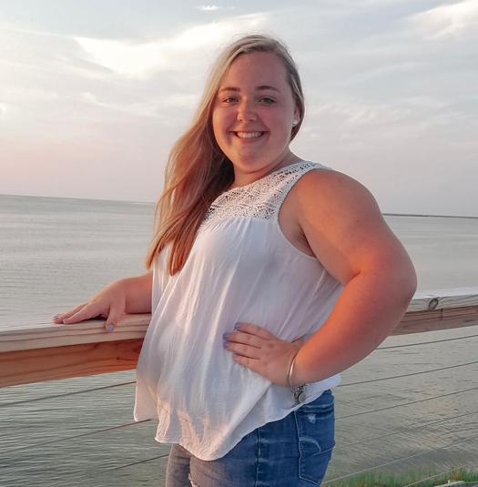 A blonde woman leaning on a pier near the ocean.