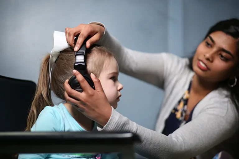 A former Marywood student helps a child put on headphones